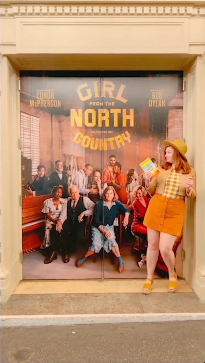 Creator posing beside the Girl From the North Country theatre artwork.